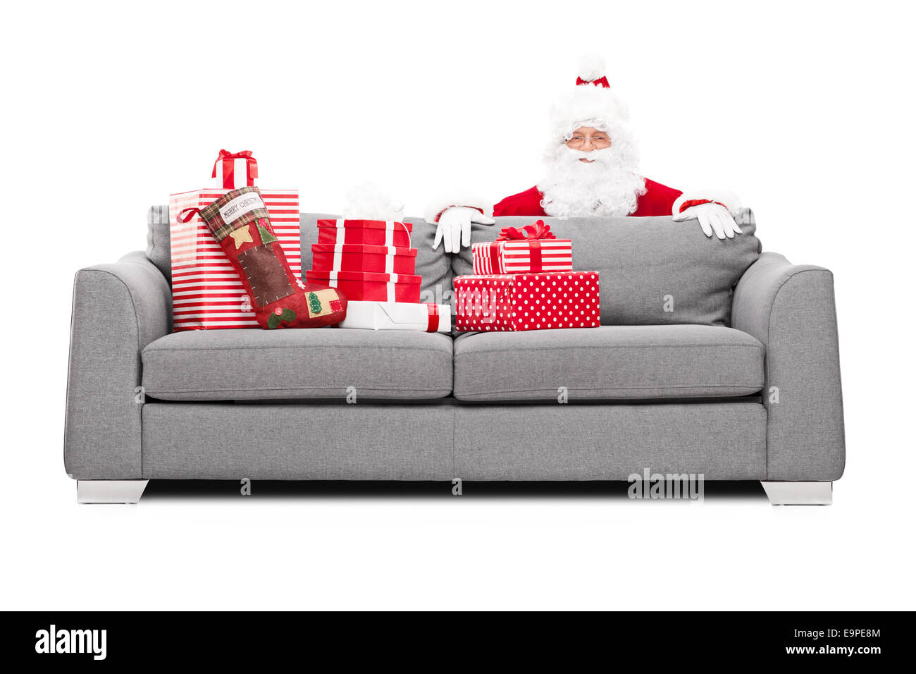 Santa Claus versteckt sich hinter einem Sofa voller Weihnachtsgeschenke isoliert auf weißem Hintergrund Stockfoto