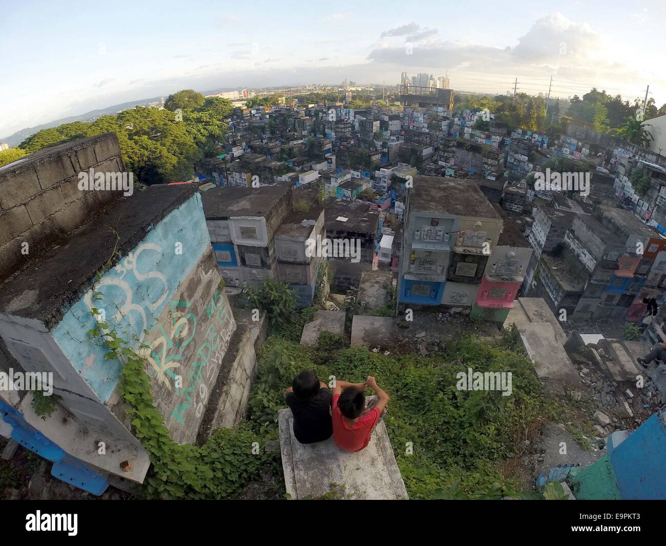 Marikina City, Philippinen. 31. Oktober 2014. Kinder sitzen auf einem Grab am Tag vor Allerheiligen auf dem Friedhof in Marikina City, Philippinen, am 31. Oktober 2014. Millionen von Menschen zu Ehren der Toten durch ihre verstorbenen Verwandten auf verschiedenen Friedhöfen in Allerheiligen und Allerseelen auf den Philippinen zu besuchen. © Rouelle Umali/Xinhua/Alamy Live-Nachrichten Stockfoto