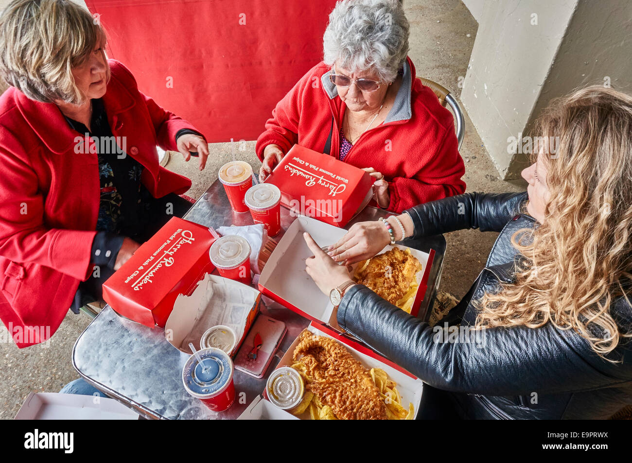 Drei Generationen von Frauen, die bereit waren, Fisch und Chips zu essen, an einem Tisch sitzen, außerhalb Harry Ramsdens neben Strand von Bournemouth, Dorset, England, UK. Stockfoto