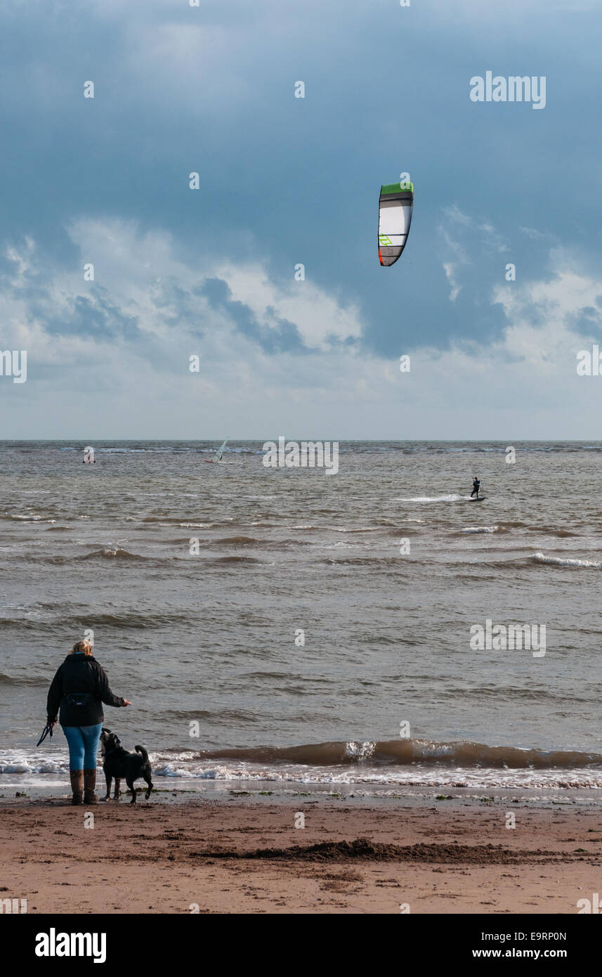 Ein Kitesurfer an einem windigen Tag in Exmouth in Devon, England. Gute Bedingungen zum Kitesurfen. Eine Frau und ihr Hund zu sehen, vom Strand entfernt Stockfoto