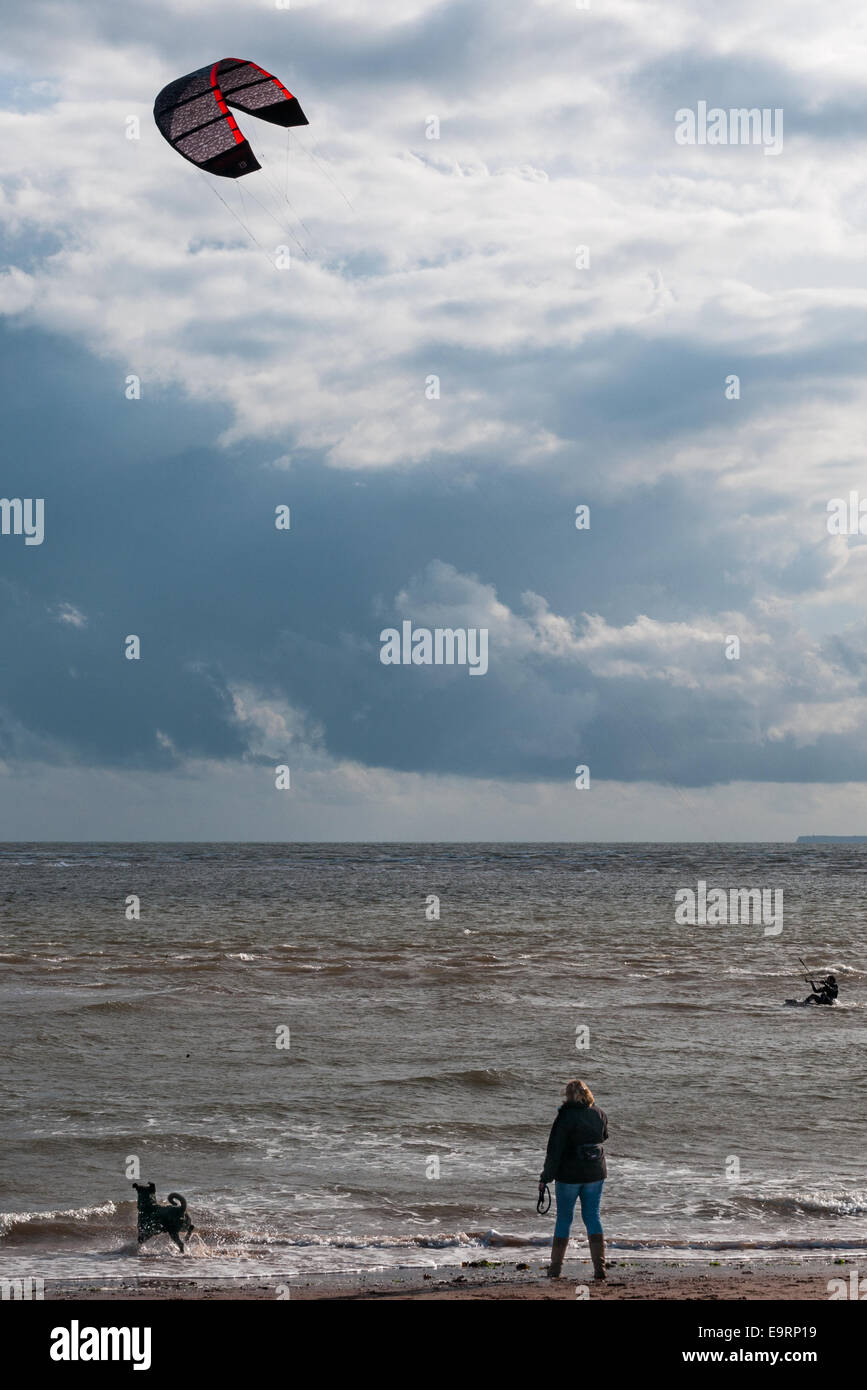 Ein Kitesurfer an einem windigen Tag in Exmouth in Devon, England. Gute Bedingungen zum Kitesurfen. Eine Frau und ihr Hund zu sehen, vom Strand entfernt Stockfoto