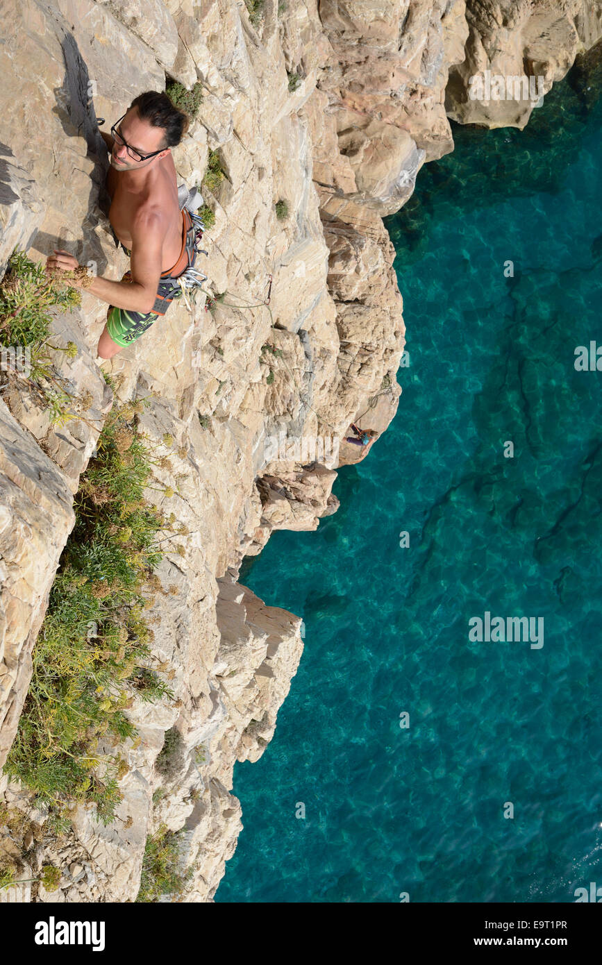 Junger Kletterer auf einer Klippe hoch über dem azurblauen Mittelmeer. Capo Noli, Provinz Savona, Ligurien, Italien. Stockfoto