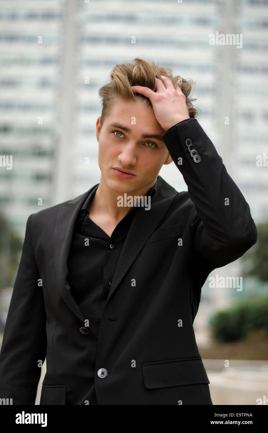 Hübscher blonder junger Mann im Freien, inmitten der Stadt, berühren Haare mit der Hand, im Business-Anzug Stockfoto