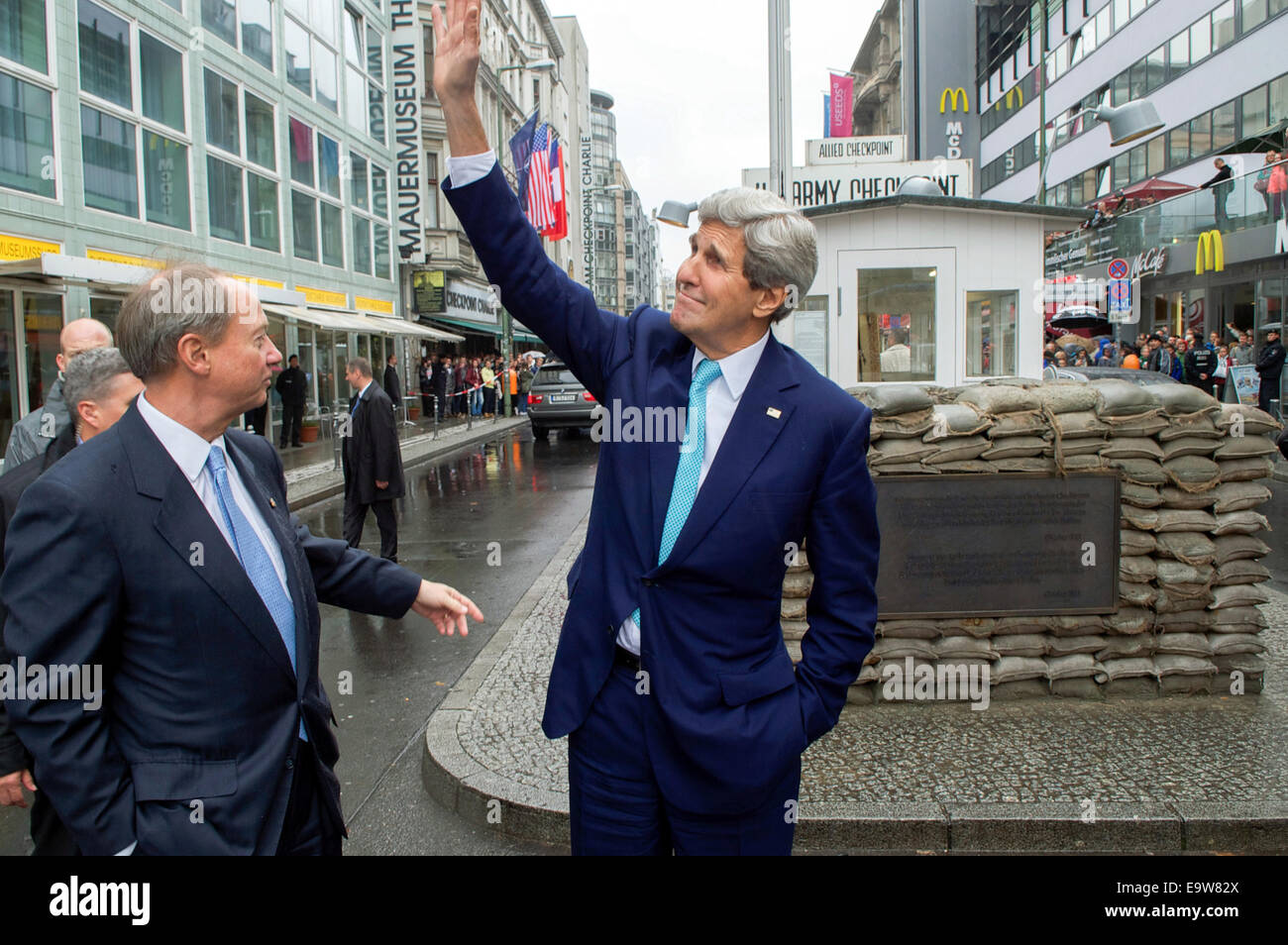US-Außenminister John Kerry winkt Büroangestellte Blick durch ihre Fenster auf ihn wie Checkpoint Charlie er besucht während einer Tour durch Berlin, Deutschland, am 22. Oktober 2014, nach einem Ereignis an den 25. Jahrestag des Mauerfalls begehen die werden Stockfoto
