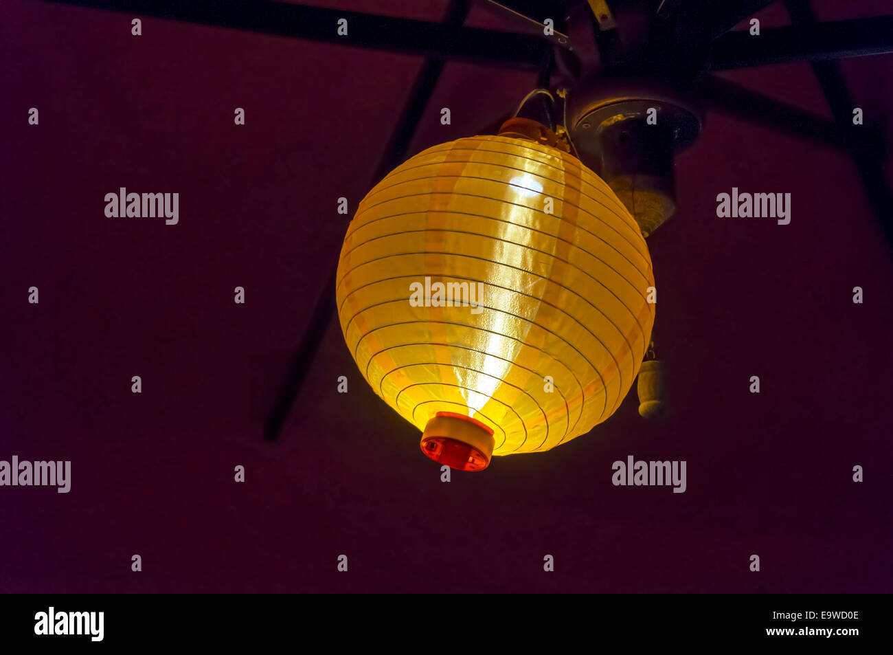 Rund um Seide chinesische oder japanische gerippte Globus leuchtet Laterne Schatten unter einer Terrasse Dach hängen ein helles Gelb in der Dunkelheit. Stockfoto