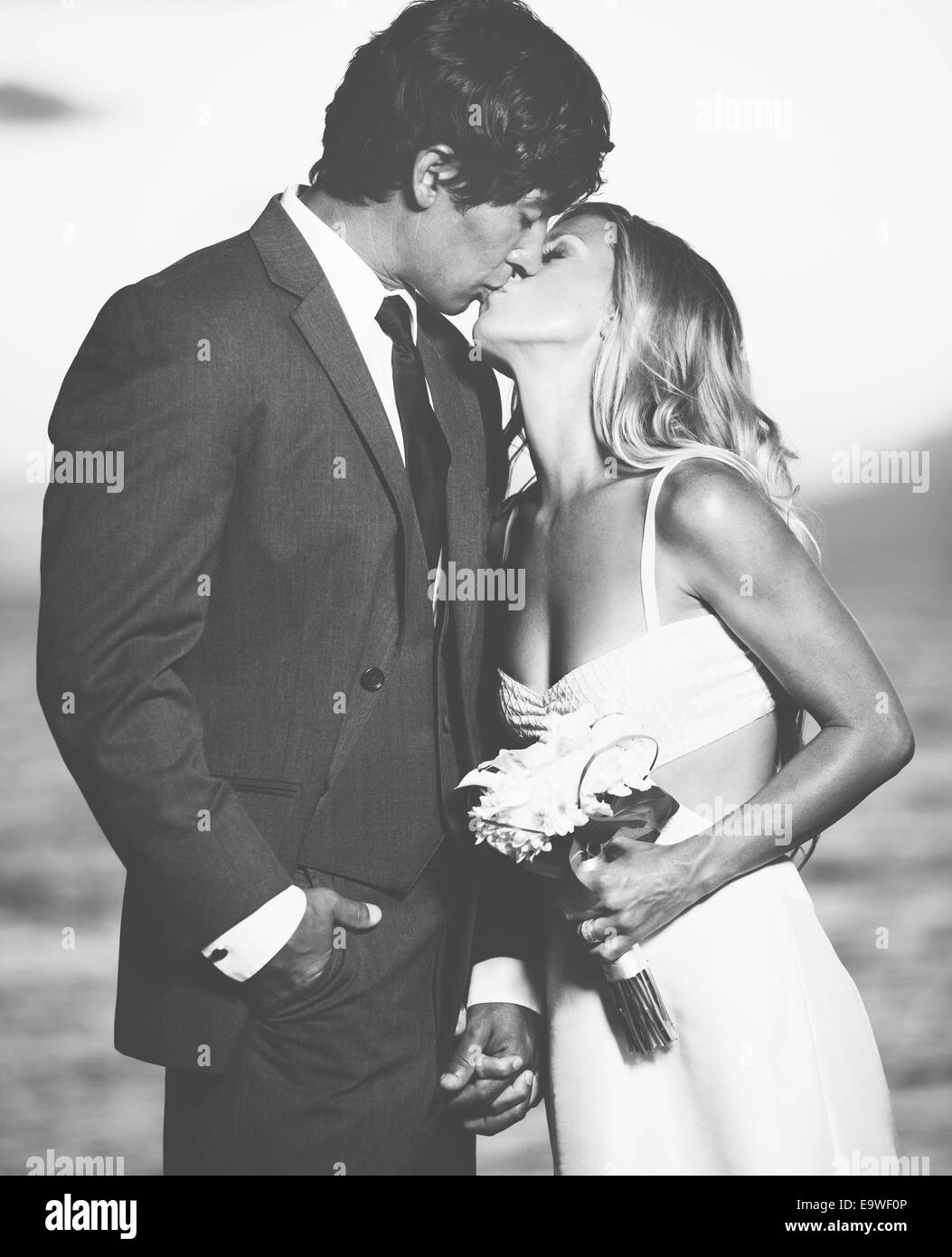 Schöne Hochzeitspaar, Braut und Bräutigam küssen am Strand bei Sonnenuntergang. Schwarz / weiß Foto Stockfoto
