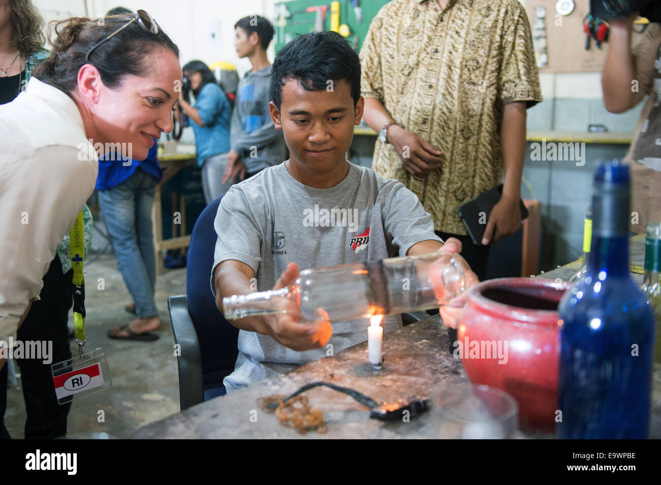 Deutsche Schauspielerin Natalia Wörner (L) schaut zu, wie ein Junge eine Glasflasche in einer Lehrwerkstatt in Jakarta, Indonesien, 3. November 2014 prägt. Die Werkstatt fertigt Kunstwerke von Ald-Glas-Flaschen und Vasen gemacht. Woerner unterstützt Deutsches Kinderhilfswerk "Kindernothilfe", die ein Kinderdorf in Jakarta, unterstützen wo ehemalige Straßenkinder Kenntnisse in Hygiene und Kochen unterrichtet werden. Nach das indonesische Ministerium für soziale Angelegenheiten Leben mehr als 11000 Kinder auf den Straßen Jakartas. Foto: Maurizio Gambarini/dpa Stockfoto