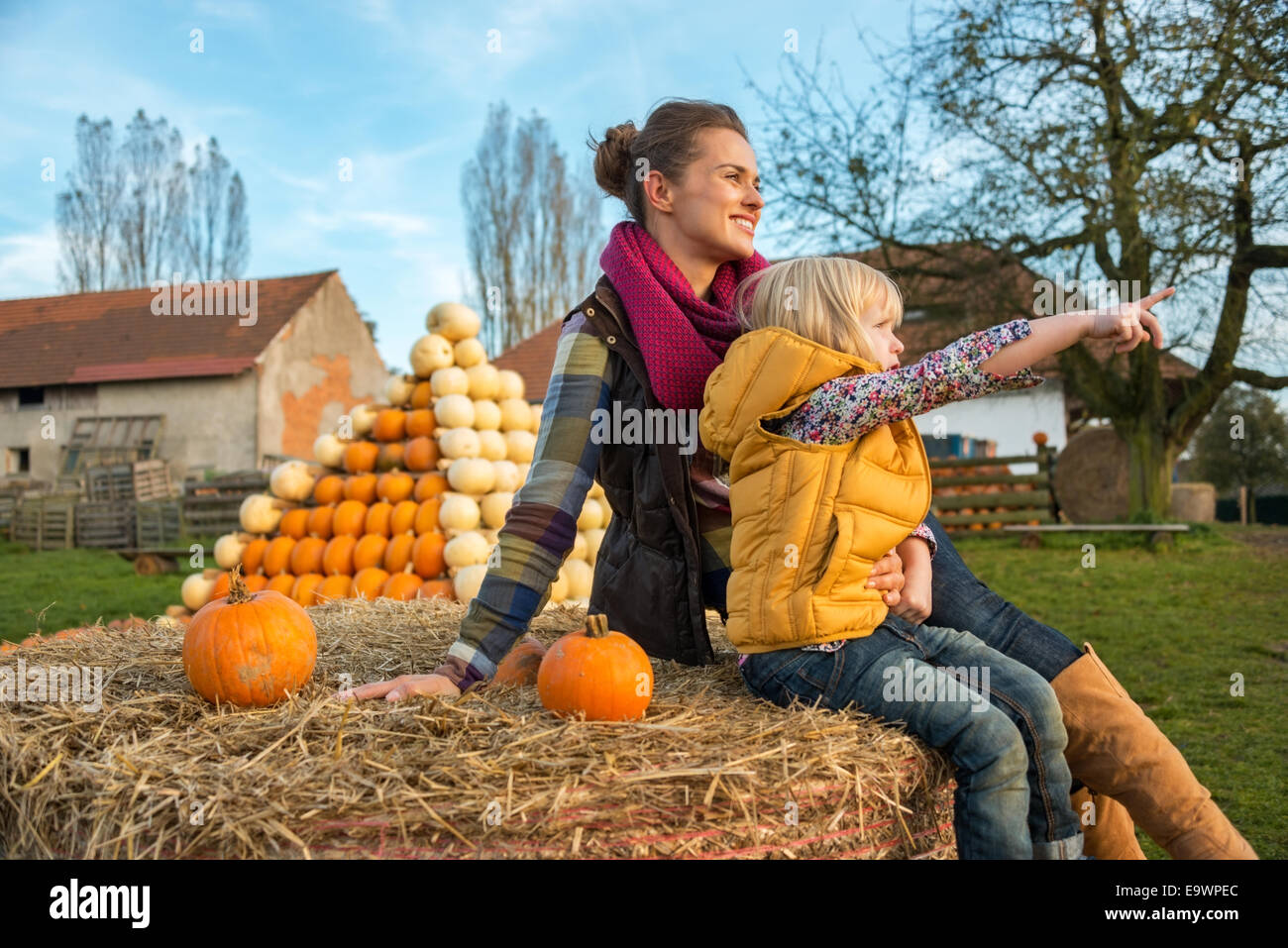 Mutter und Kind sitzen auf Heuhaufen mit Kürbissen und zeigen Stockfoto