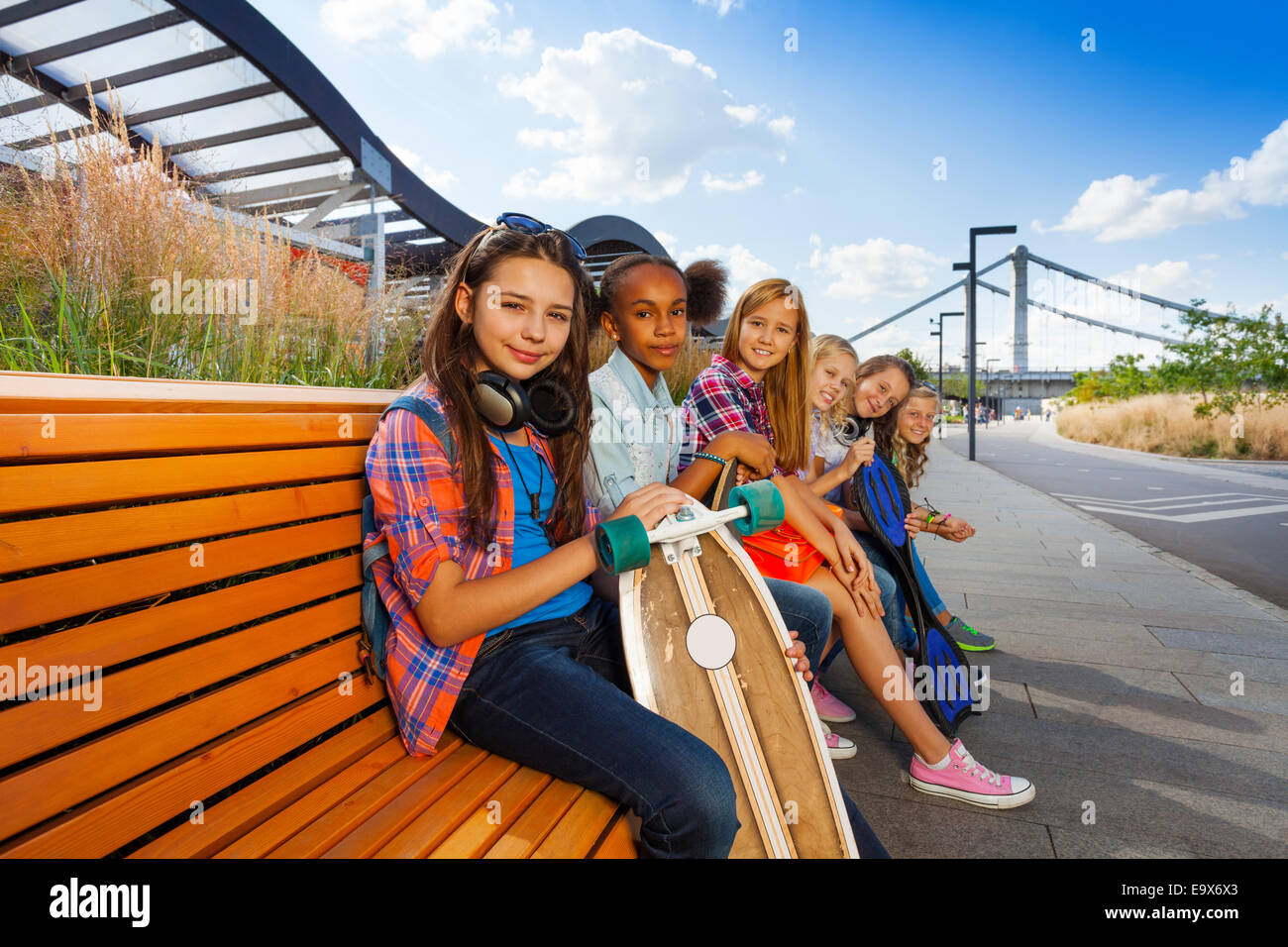 Positive Mädchen mit Skateboards sitzen auf lange Bank Stockfoto