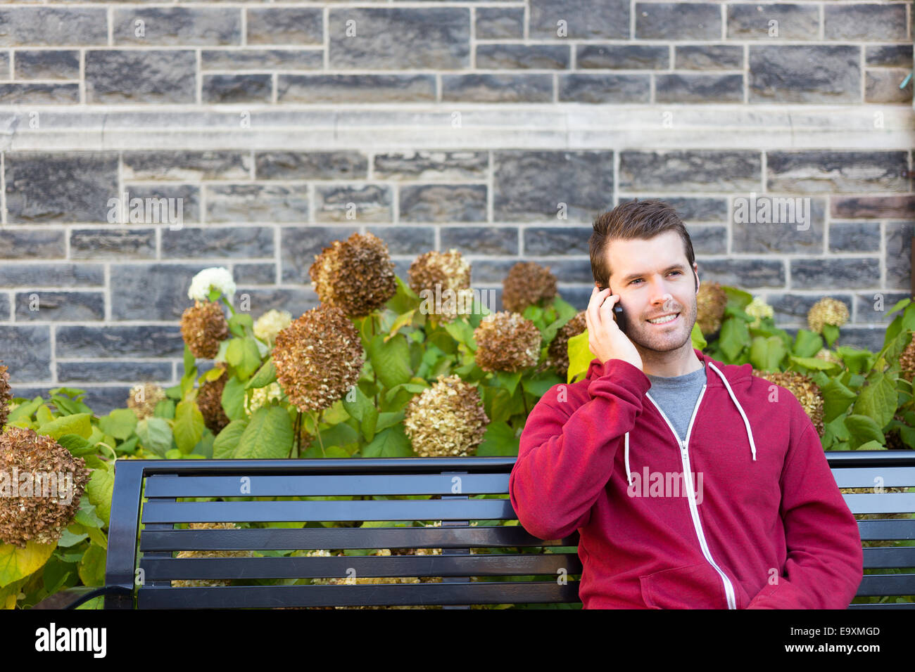 Ein Mann sitzt auf einer Bank außen mit seinem Handy Stockfoto