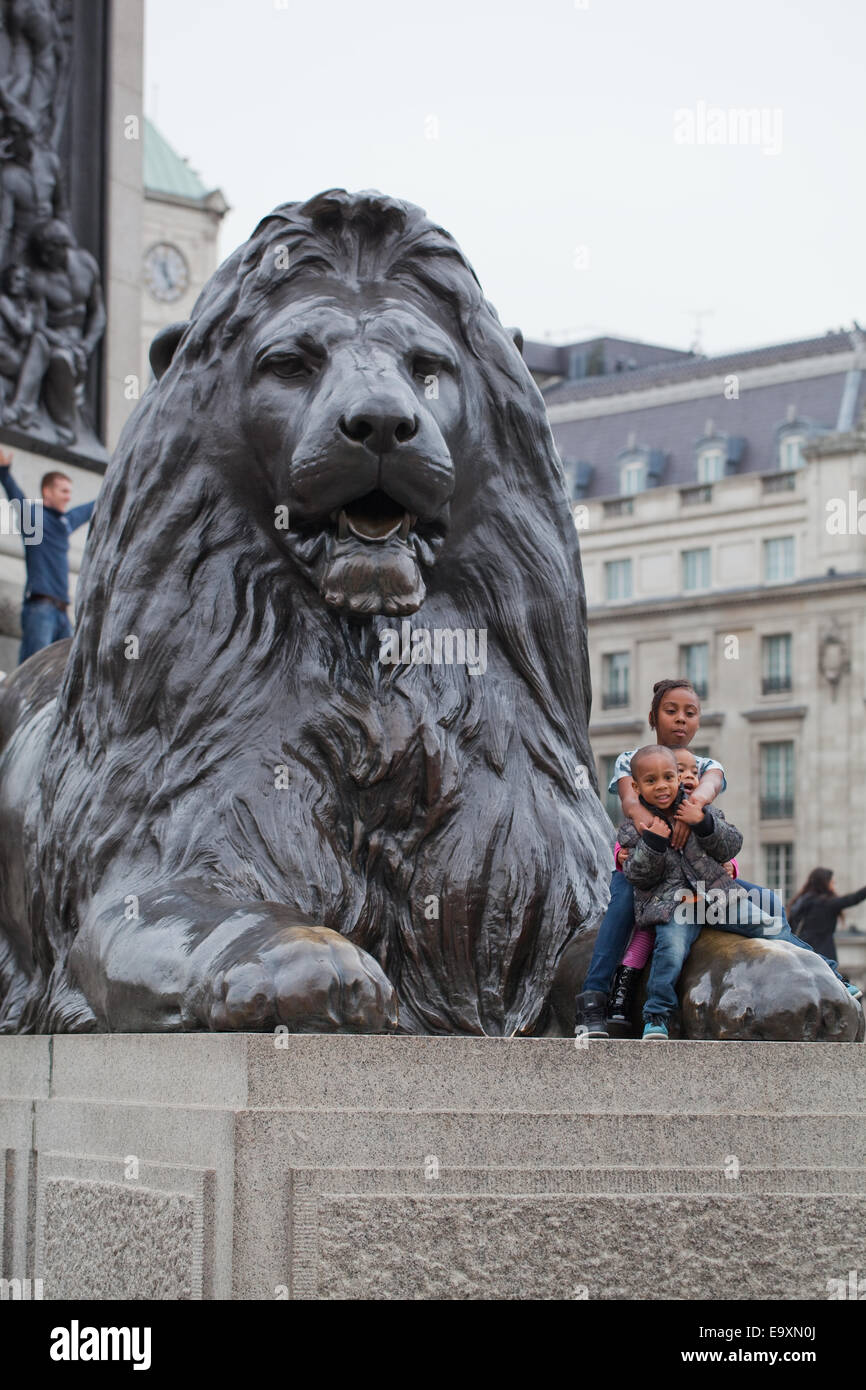 Trafalgar Square. London. England.  Ein "Landseer Löwe" auf Sockel im Vordergrund mit Afro-Karibischen Kinder posieren für Eltern Stockfoto