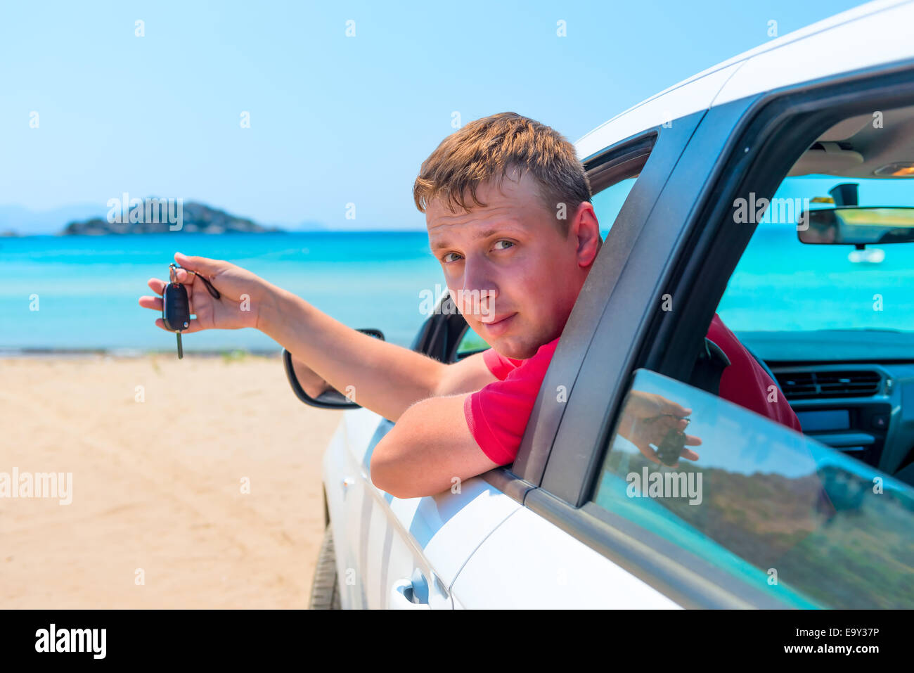 der Mann mit dem Schlüssel für das Auto schaut aus dem Fenster auf dem Hintergrund des Meeres Stockfoto