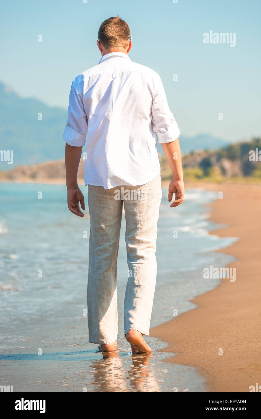 Mann in weißer Kleidung am Strand entlang spazieren Stockfoto
