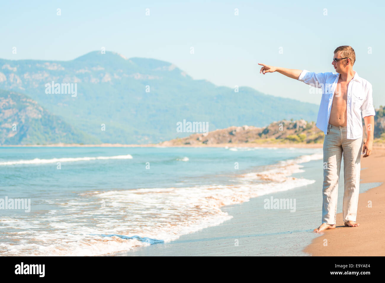 junger Mann am Strand zeigt seewärtigen Stockfoto