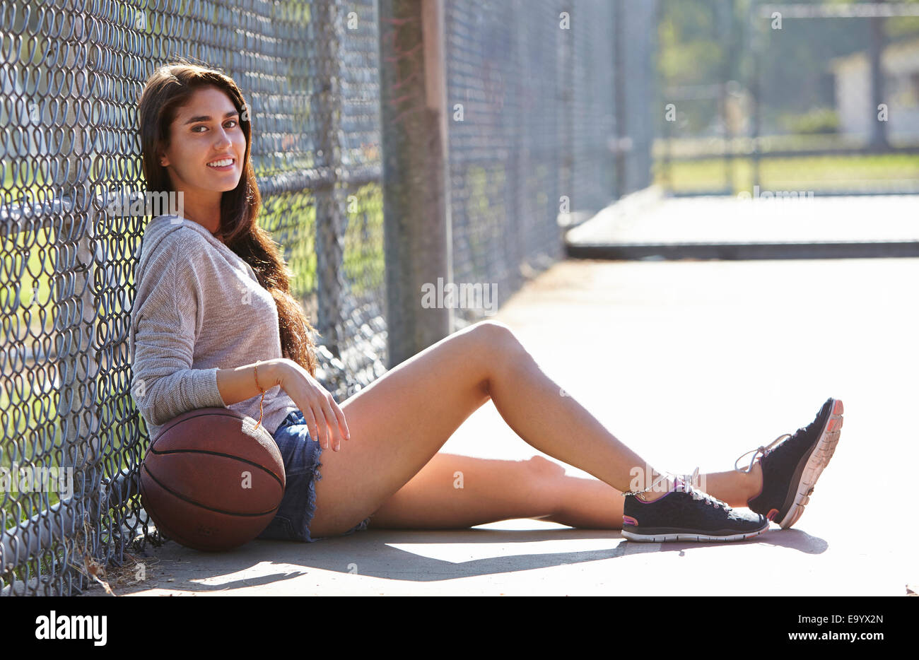 Junge Frau mit Basketball sitzen Drahtzaun Stockfoto