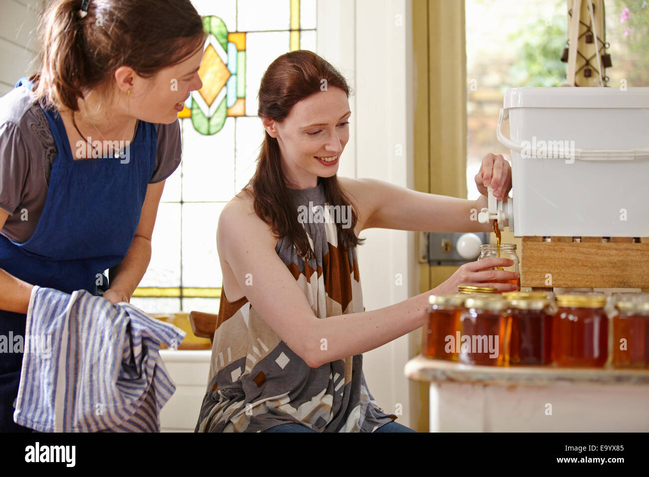 Weibliche Imker in Küche, Abfüllung gefilterten Honig aus dem Bienenstock Stockfoto