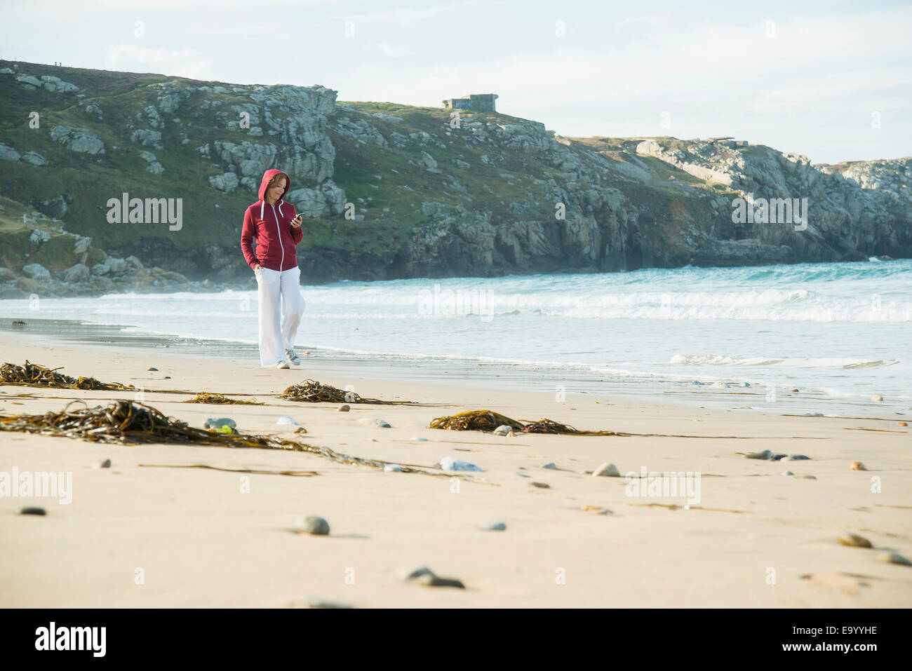 Reife Frau SMS auf Smartphone beim Spaziergang am Strand, Camaret-Sur-Mer, Bretagne, Frankreich Stockfoto