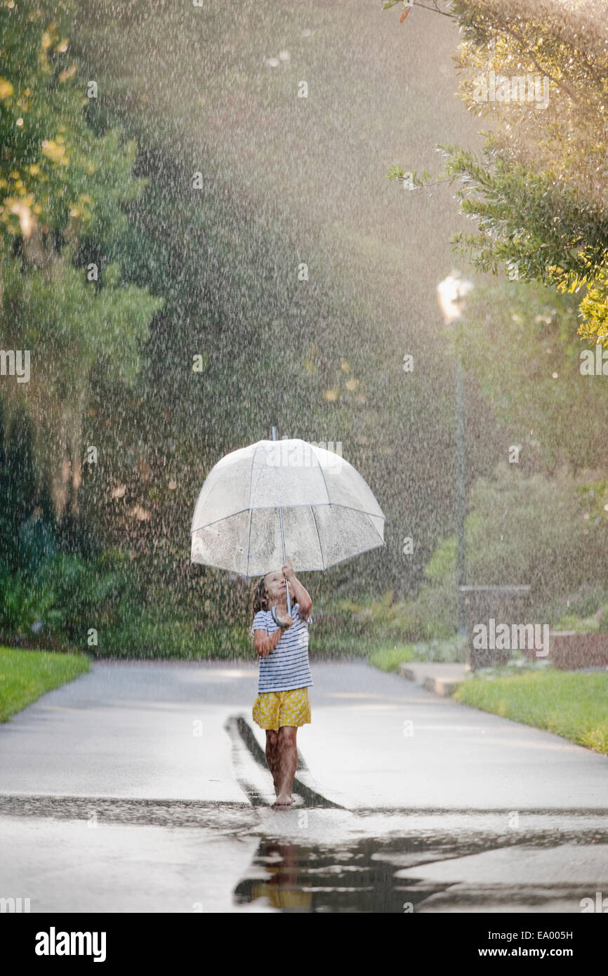 Barfuß Mädchen hält Regenschirm und gehen durch Pfützen auf der Straße Stockfoto