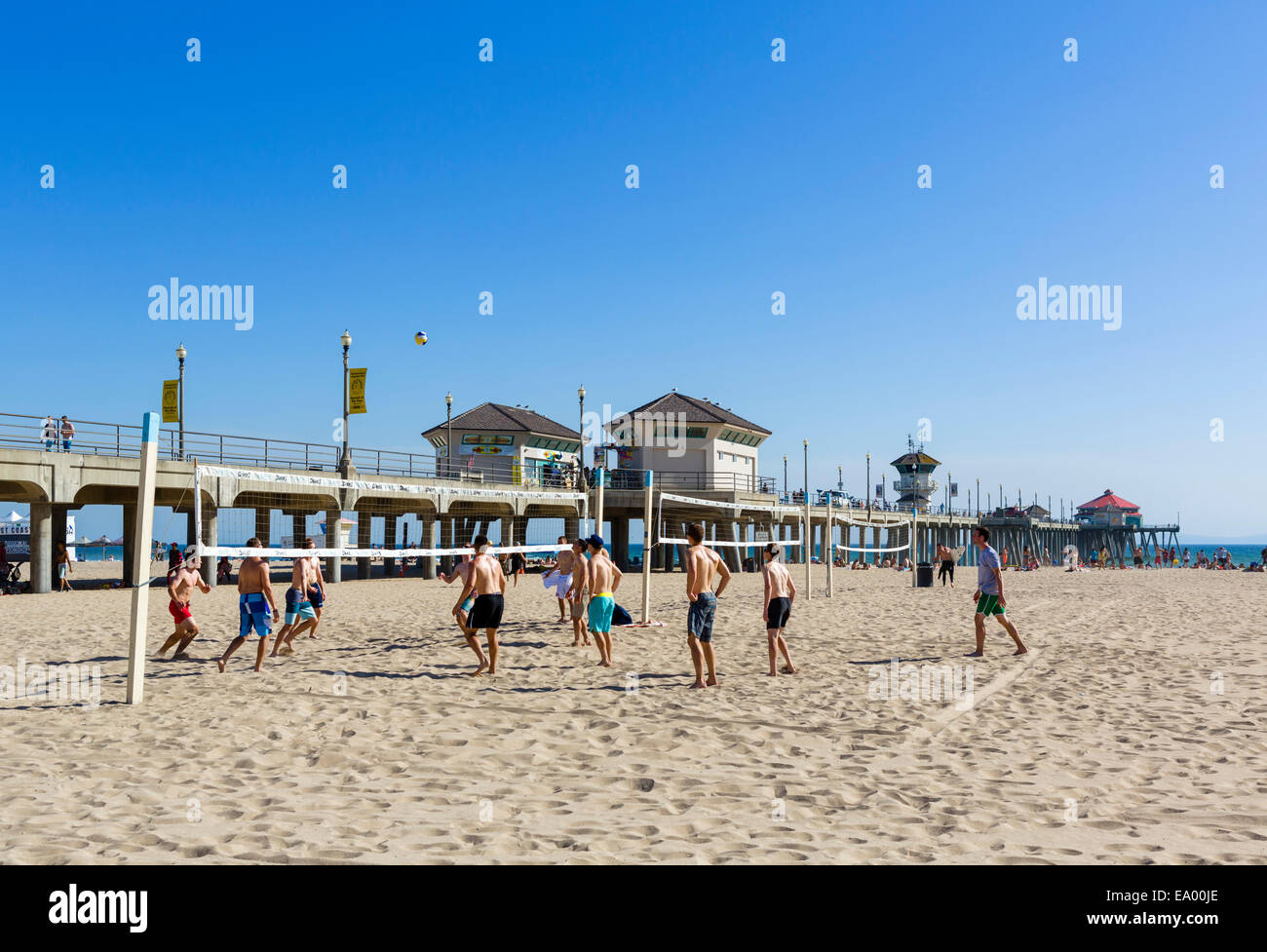 Junge Männer spielen Beachvolleyball vor dem Pier in der Innenstadt von Huntington Beach, Orange County, Kalifornien, USA Stockfoto