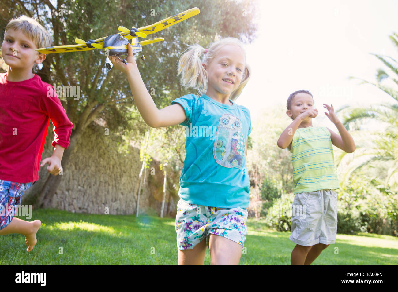 Drei Kinder im Garten laufen mit Spielzeugflugzeug Stockfoto