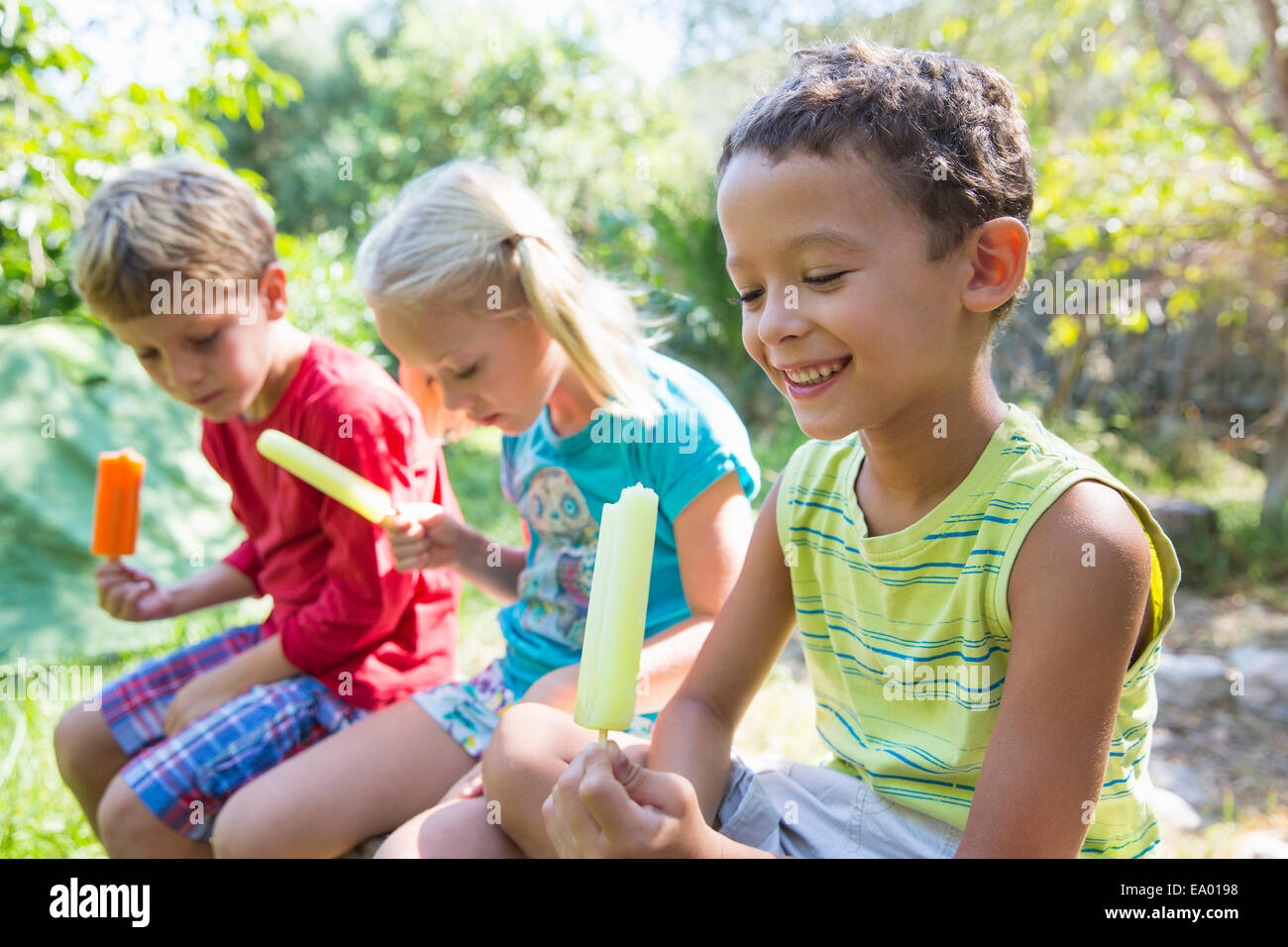 Drei Kinder im Garten essen Eis am Stiehl Stockfoto