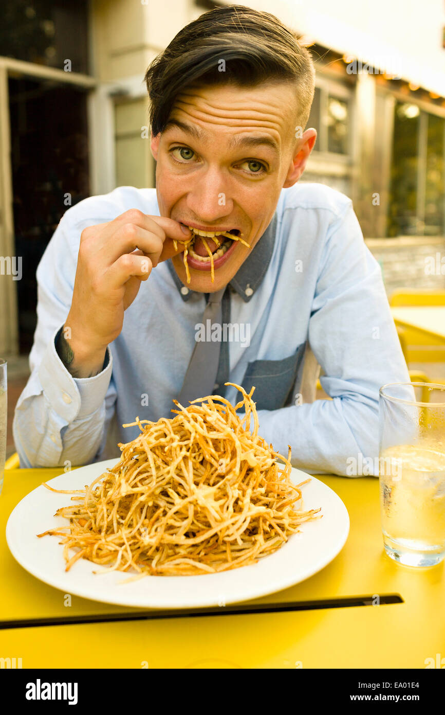 Junger Mann Essen dünne Pommes frites im Straßencafé Stockfoto
