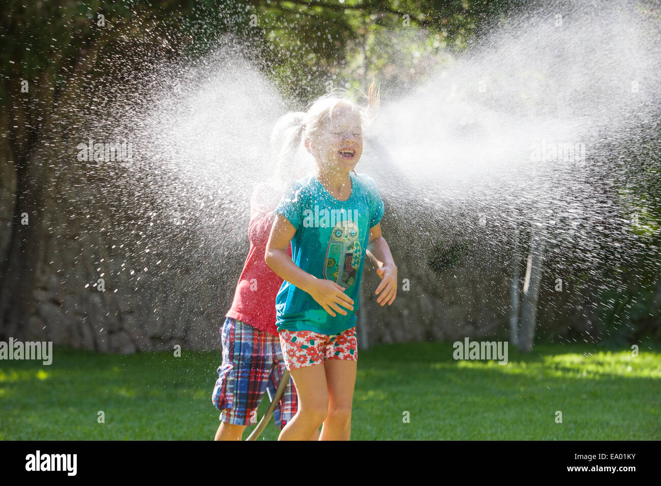 Junge Mädchen im Garten zu jagen, mit Wasser sprinkler Stockfoto