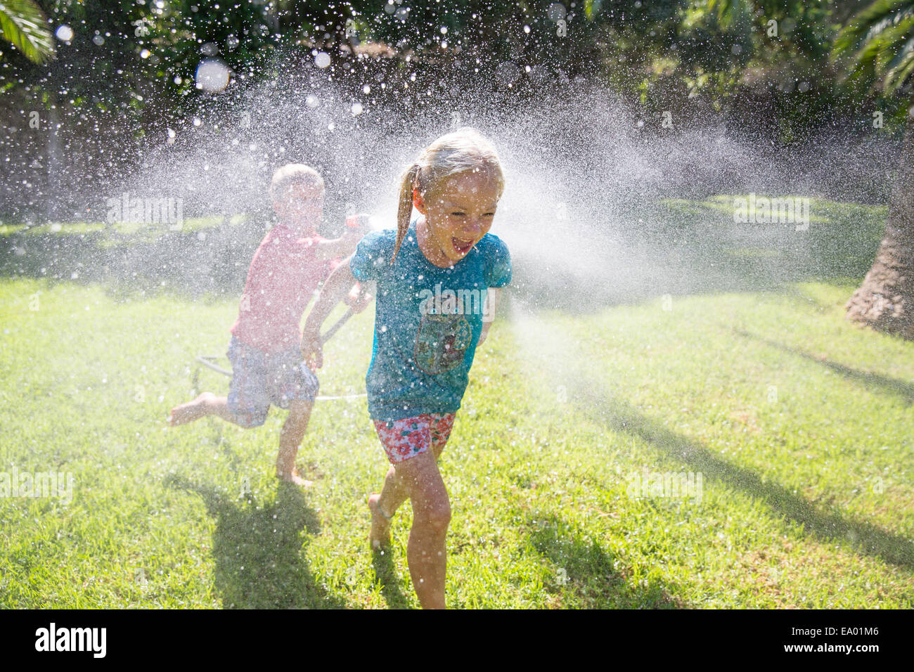Junge Mädchen im Garten mit Wasser Sprinkler nachlaufen Stockfoto