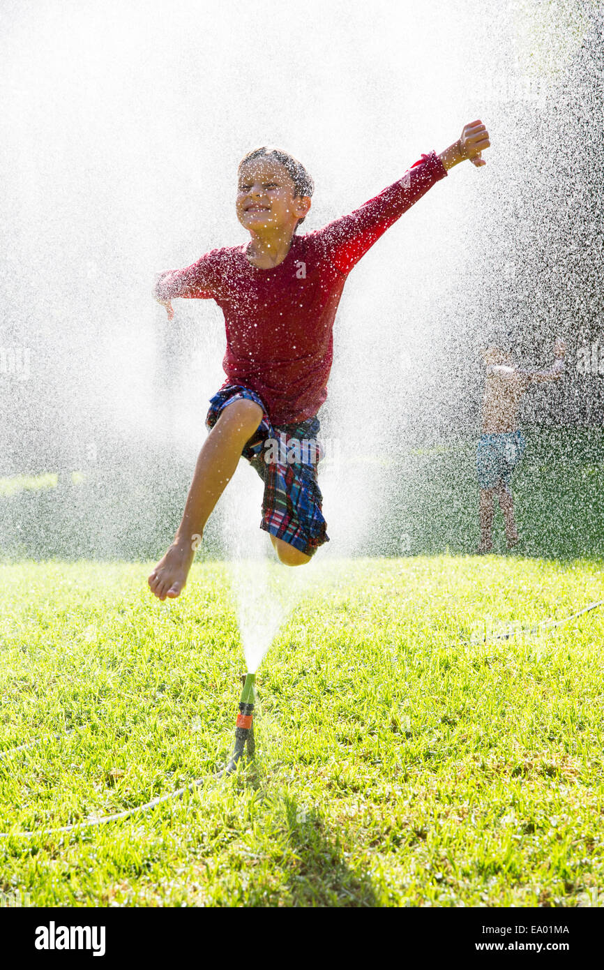 Junge, springen über Wasser Sprinkler im Garten Stockfoto