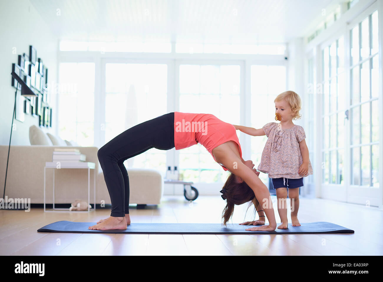 Mitte Erwachsene Mutter praktizieren Yoga mit neugierigen Kleinkind Tochter Stockfoto