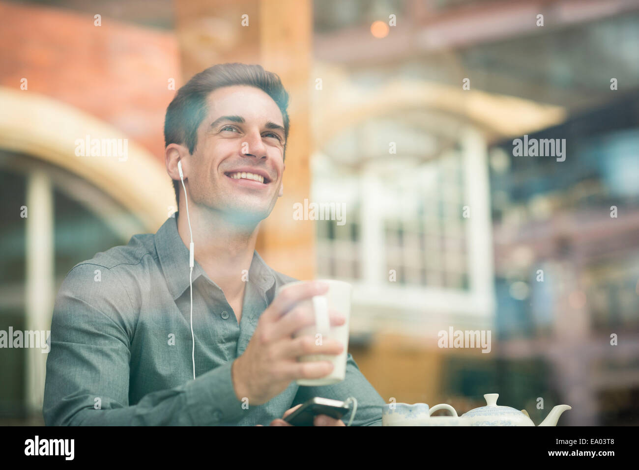 Junger Geschäftsmann hören Kopfhörer im Café Fensterplatz, London, UK Stockfoto