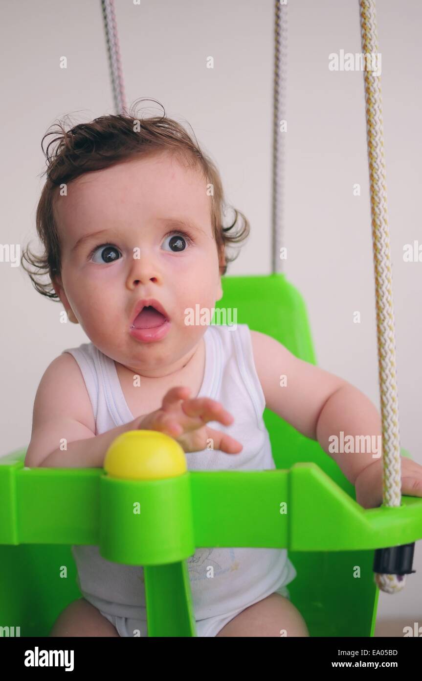 Baby mit weißen Oberteil auf eine grüne Schaukel. Kaukasischen, braune Augen. Stockfoto