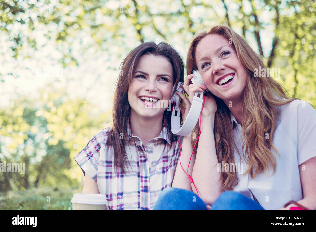 Zwei junge Freundinnen Kaffee trinken und Freigeben von Musik über Kopfhörer im park Stockfoto
