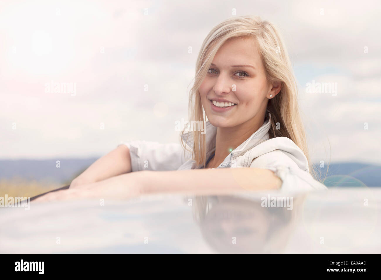 Junge Frau lächelnd neben Auto Stockfoto
