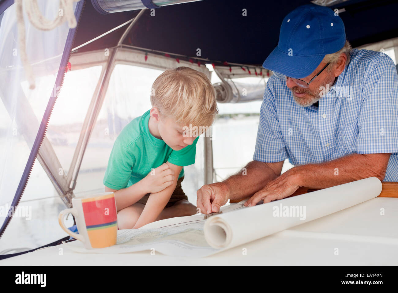 Junge und Großvater Planung auf Navigationskarten im Segelboot-Kabine Stockfoto