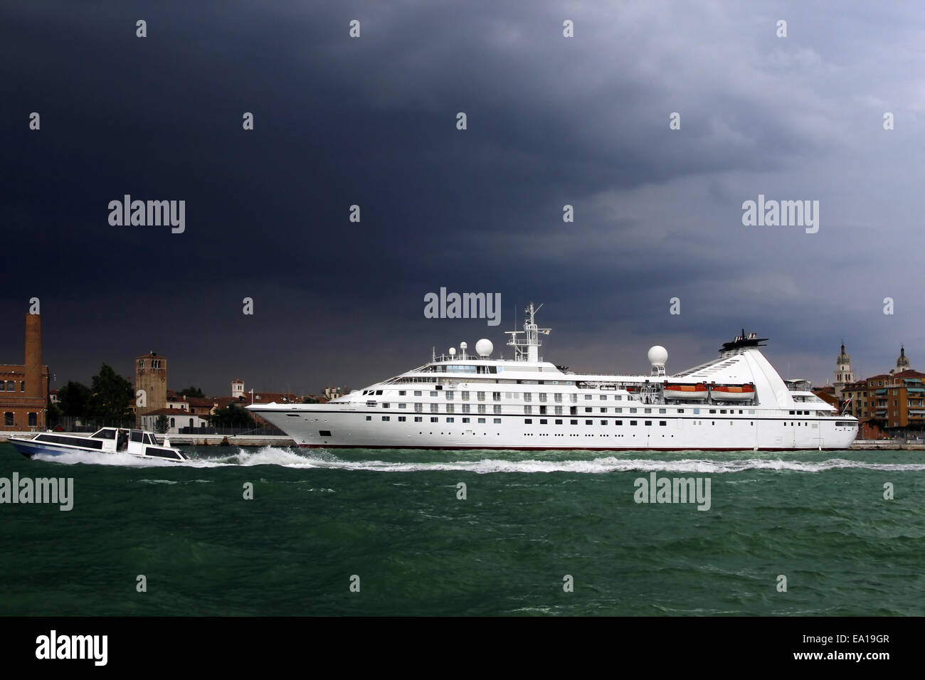 Großes Kreuzfahrtschiff und kleine Wasser-Taxi unter Gewitterhimmel, Venedig, Italien. Metapher des Wettbewerbs zwischen großen und kleinen Unternehmen Stockfoto