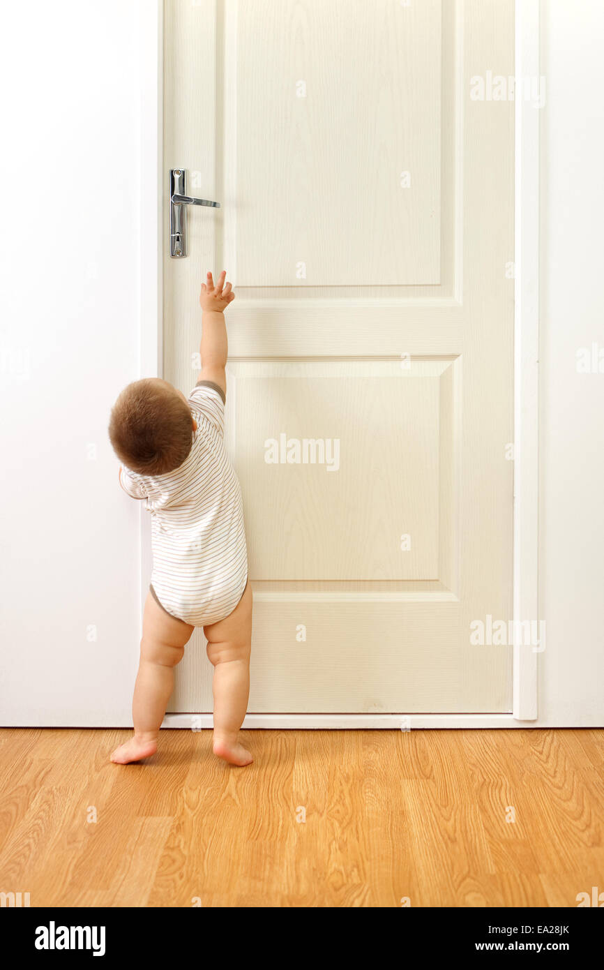 Baby Boy vor einer verschlossenen Tür versucht, das Handle zu erreichen Stockfoto