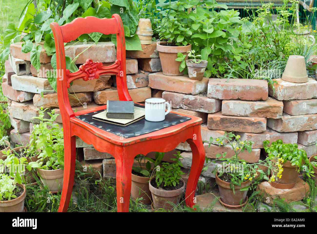 roter Stuhl in einem Garten mit Kräutern, Tasse und Bücher Stockfoto