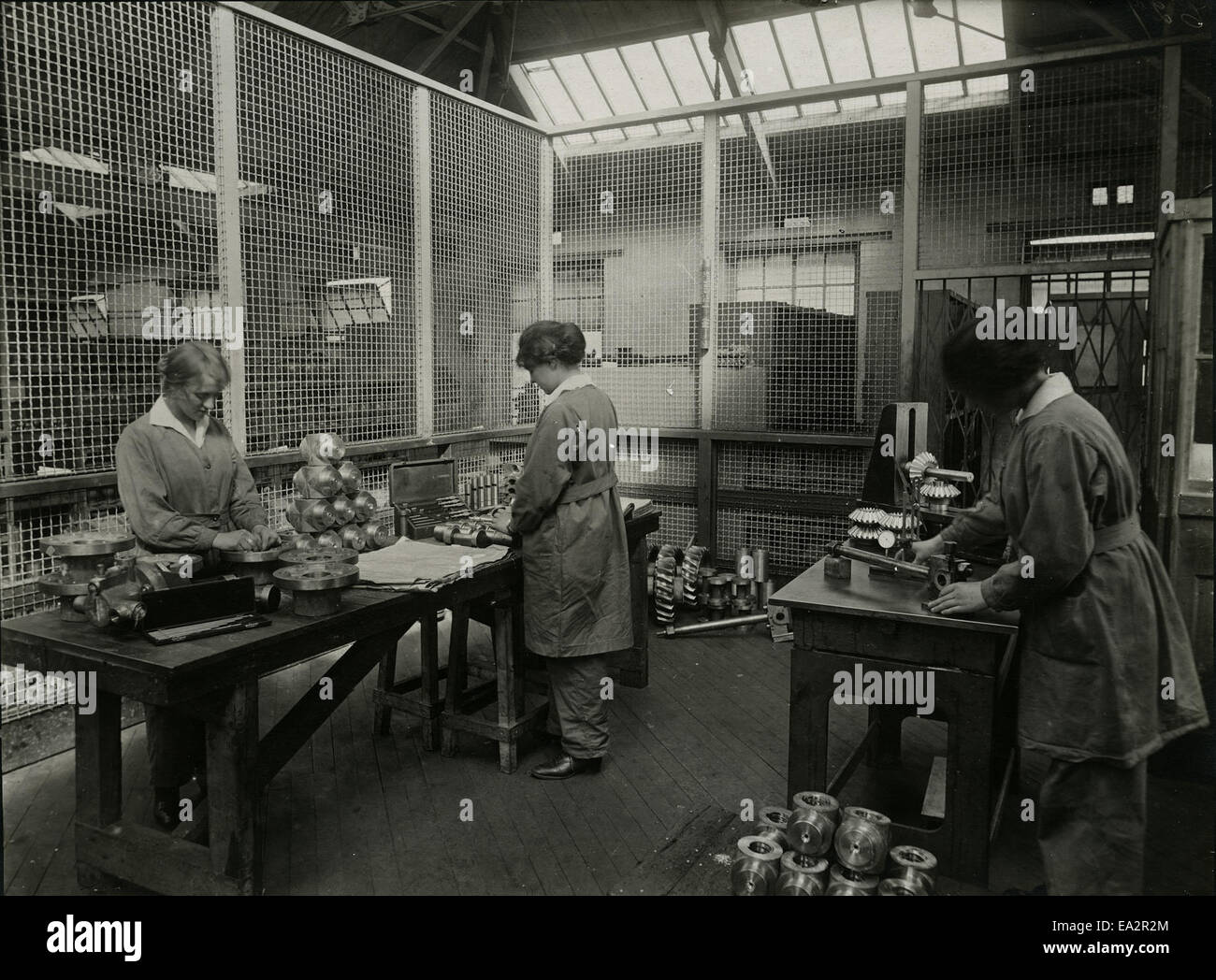 Die Abbildung zeigt eine Gruppe von Frauen, die Motorenteile sorgfältig inspizieren. Diese Szene spiegelt den Beitrag von Frauen in technischen und mechanischen Bereichen in einer Zeit wider, als ihre Rolle in solchen Branchen immer größer wurde. Stockfoto