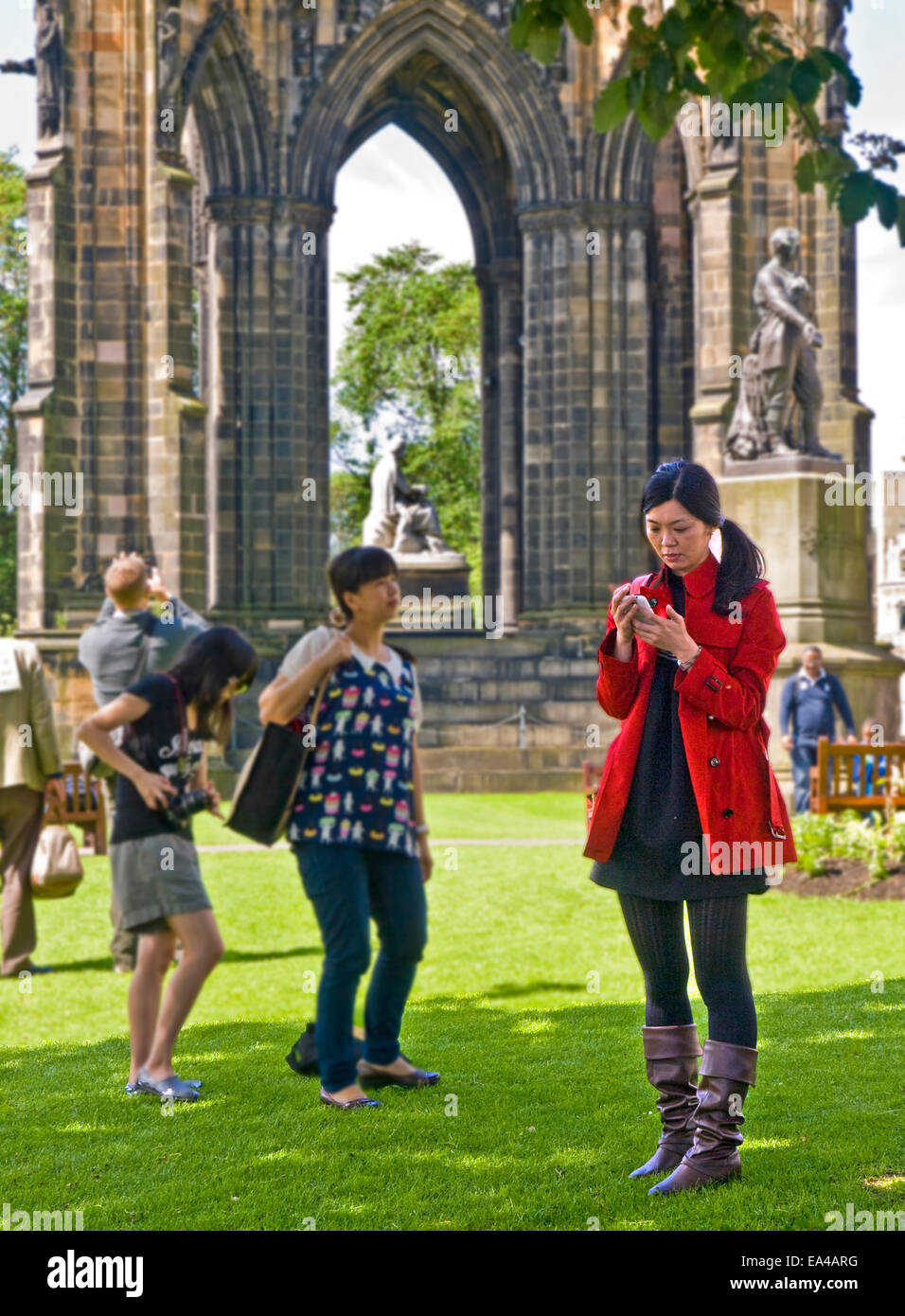 Eine junge Frau, die Überprüfung ihres Mobiltelefons unter Gruppe von Touristen vor dem Scott-Denkmal in Edinburgh Stockfoto