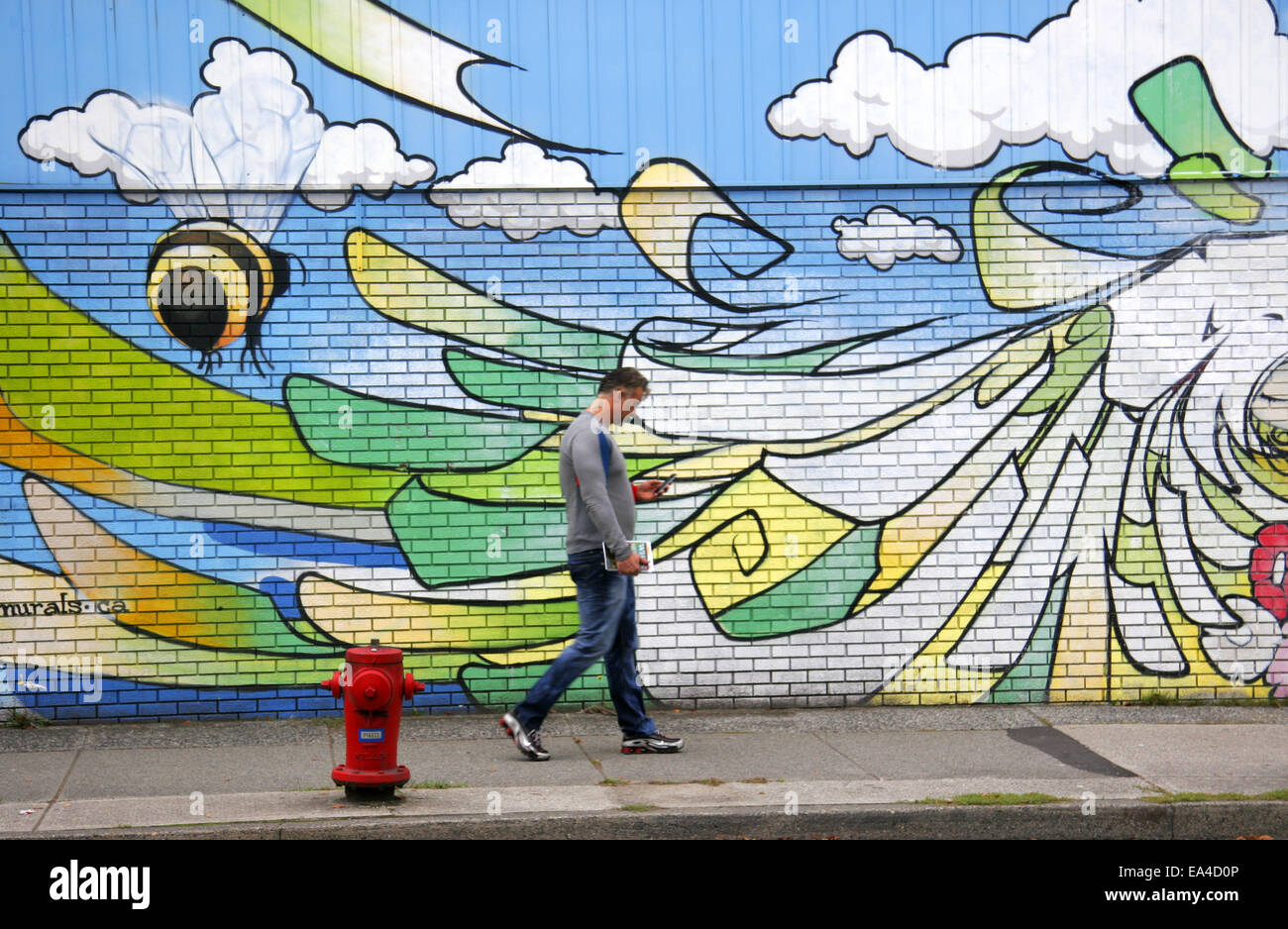 Mann, spazieren, vorbei an einem Wandbild in der Nähe von Main Street, Vancouver, Kanada Stockfoto