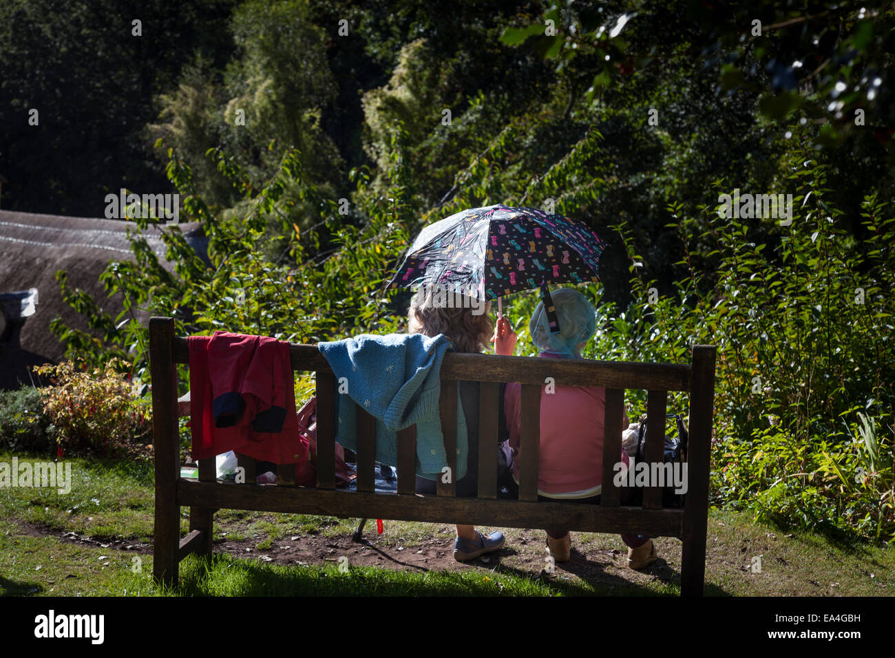 Zwei ältere Damen Schatten selbst Form der Sonne mit einem Regenschirm während sitzen und im Chat außerhalb auf einer Holzbank. Stockfoto