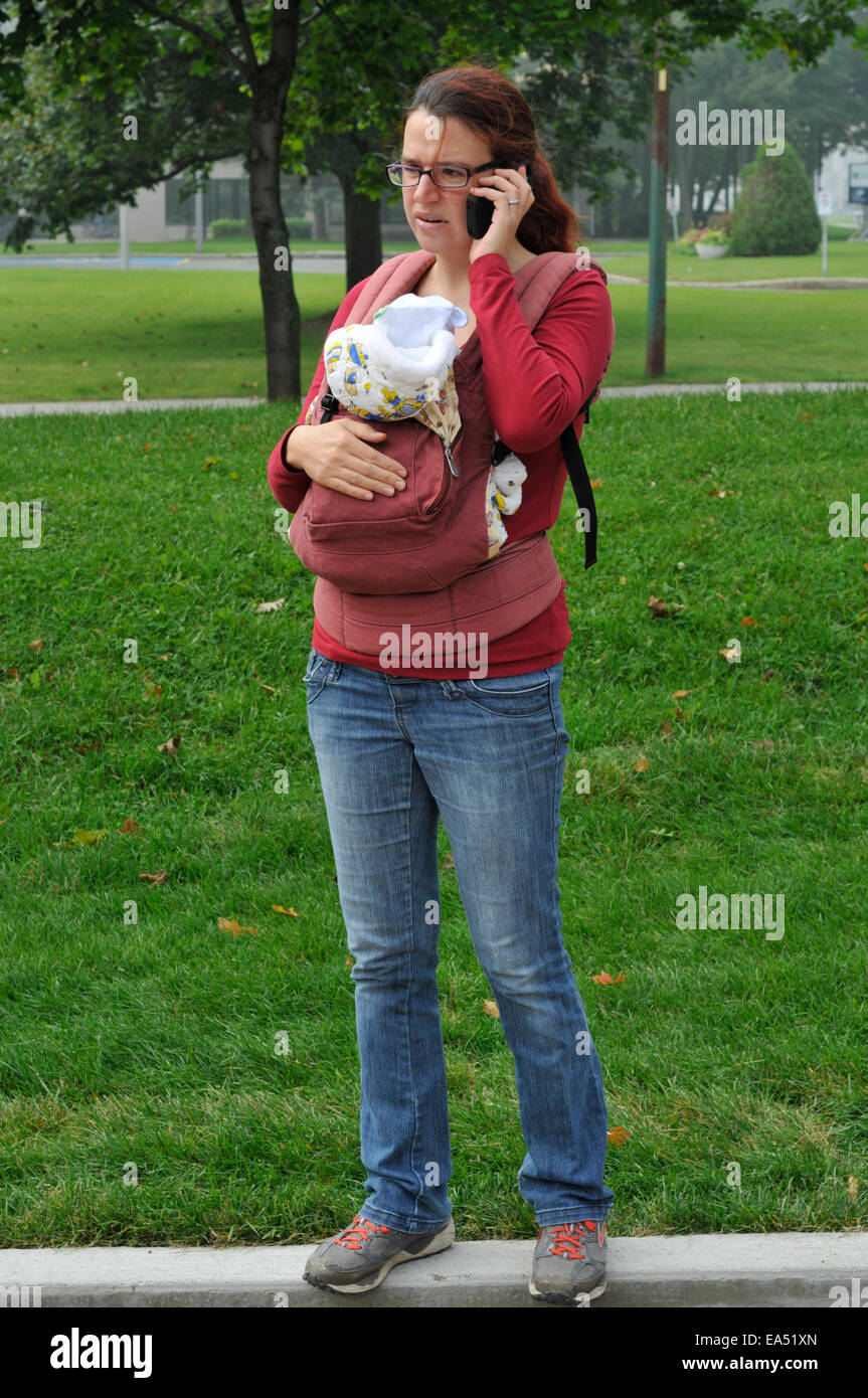Eine Mutter ein Baby zu tragen und mit Hilfe eines Mobiltelefons Stockfoto