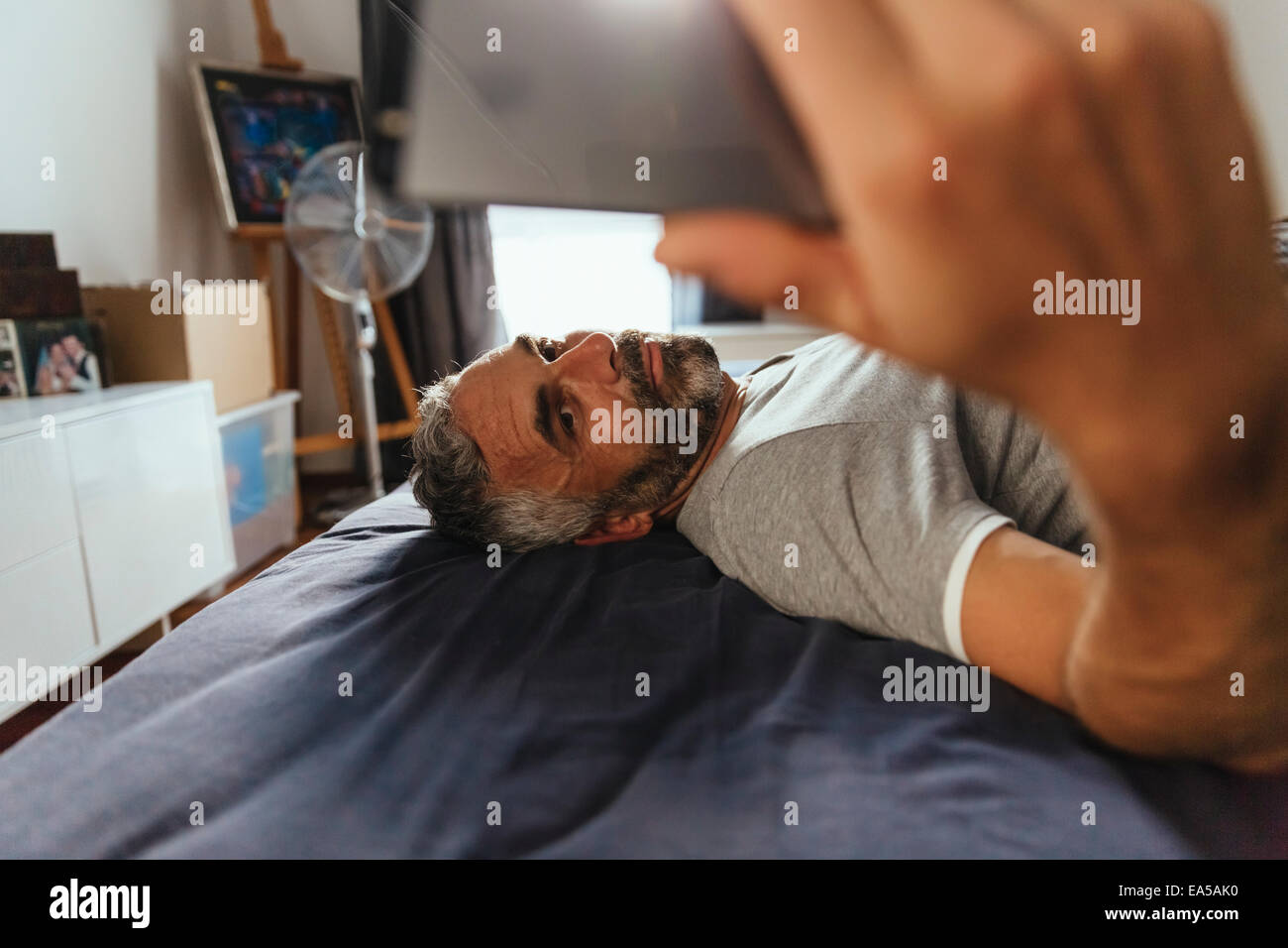 Ernst aussehender Mann liegt auf seinem Bett, wobei ein Selbstporträt mit seinem smartphone Stockfoto