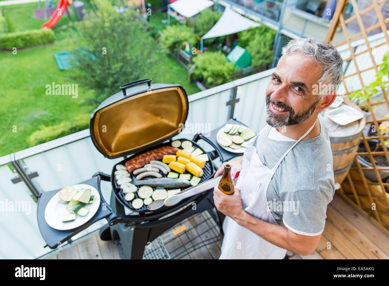 Lächelnder Mann auf seinem Balkon grillen Stockfoto