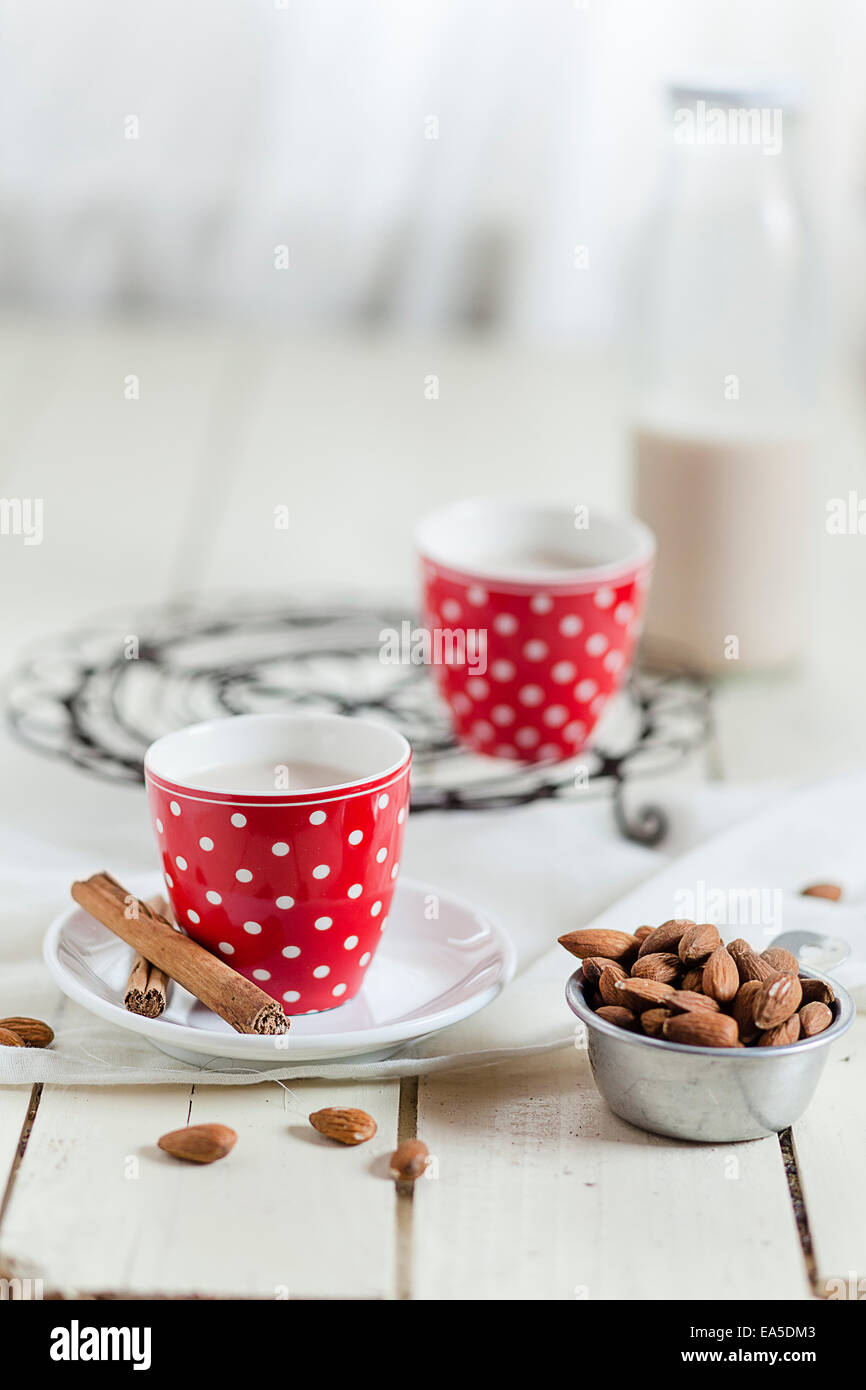 Zwei Tassen selbstgemachte Mandelmilch, Zimtstangen und eine Schüssel mit Mandeln Stockfoto