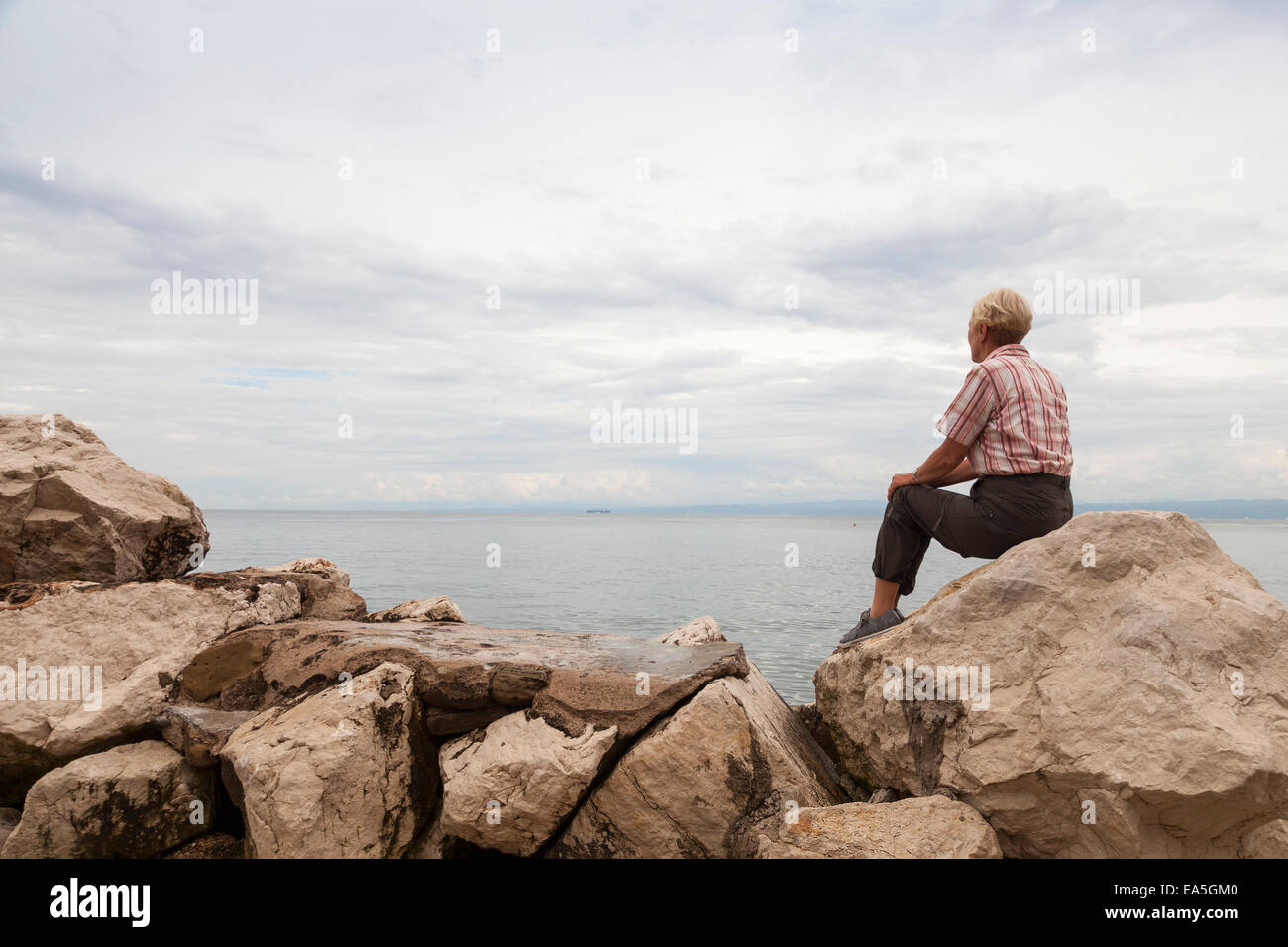 Slowenien, Piran, Frau sitzen auf den Felsen am Wasser mit Blick auf den Horizont Stockfoto
