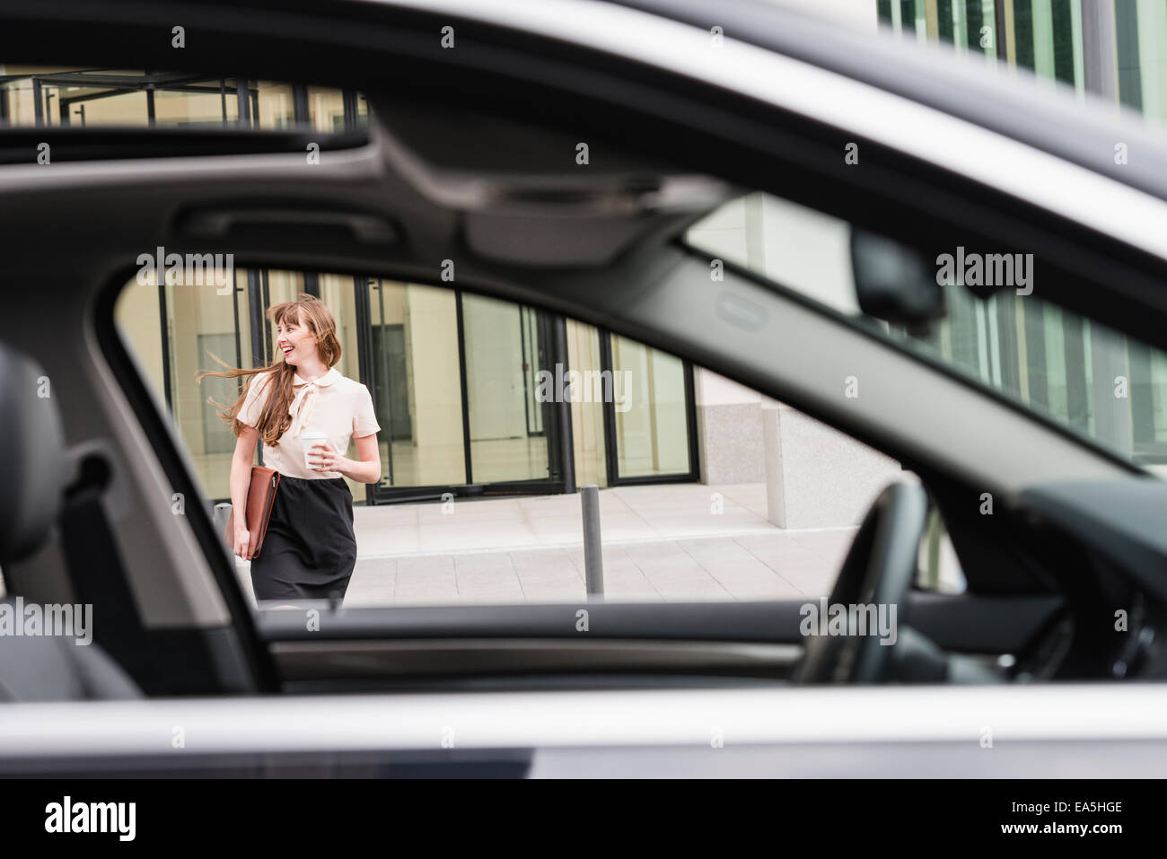 Deutschland, Hessen, Frankfurt, glücklich Geschäftsfrau zu Fuß mit Kaffee, hinter einem Auto zu gehen Stockfoto