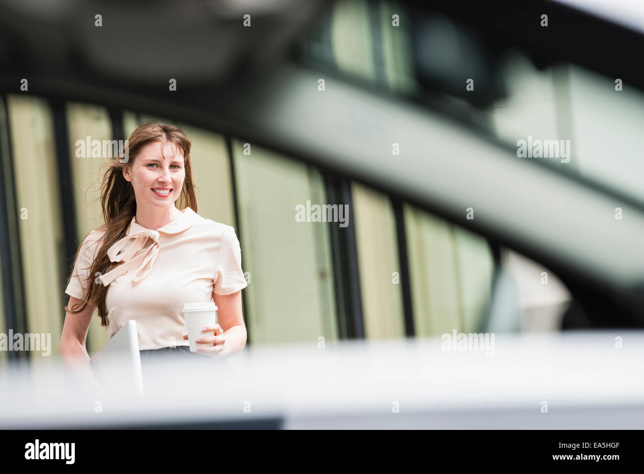Deutschland, Hessen, Frankfurt, Porträt von lächelnden Geschäftsfrau mit Kaffee, um hinter einem Auto stehend gehen Stockfoto