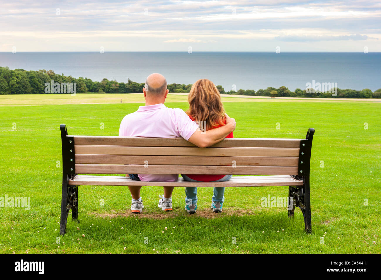 Rückansicht des mittleren Alters paar sitzt auf einer Bank mit Blick auf das Meer Stockfoto